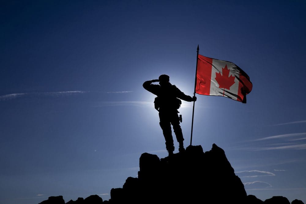 Canadian Soldier on top of mountain holding flag silhouette